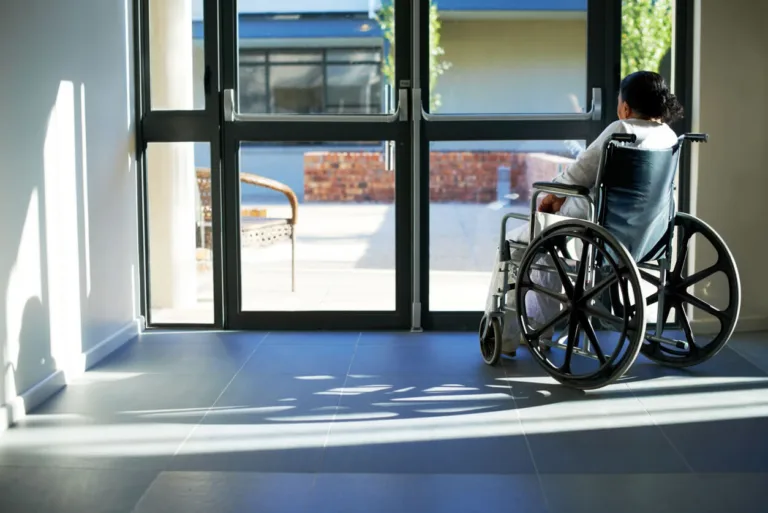 A person in a wheelchair looking out a set of glass doors from a building's interior.