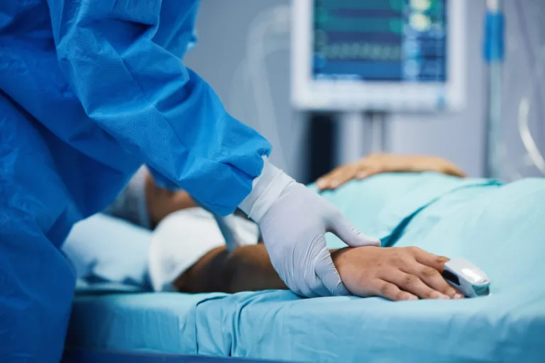 Nurse wearing gloves touching the hand of a patient on a surgical bed