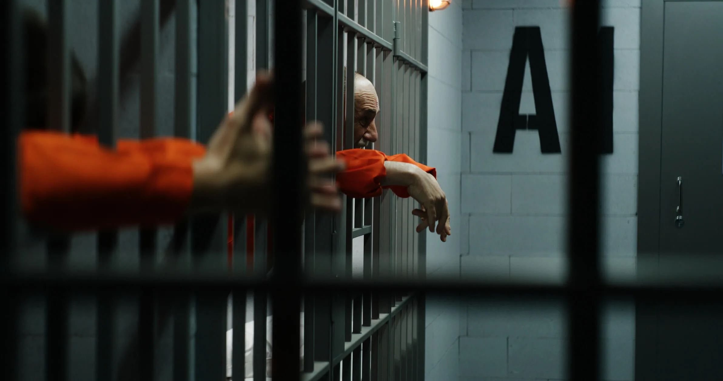 Prisoners in orange uniforms lean on metal bars in prison cells
