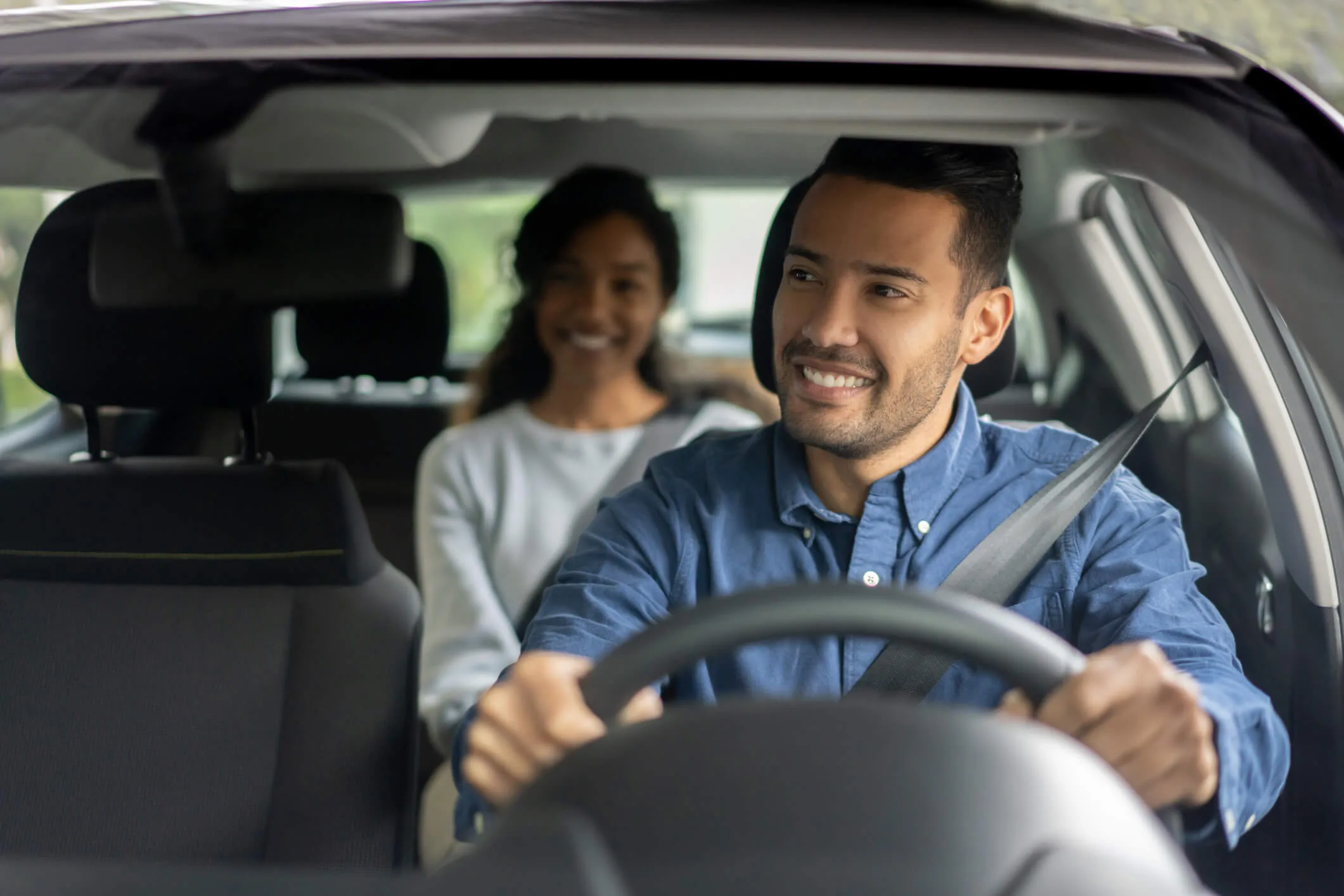 Happy Latin American rideshare driver transporting a woman in a car
