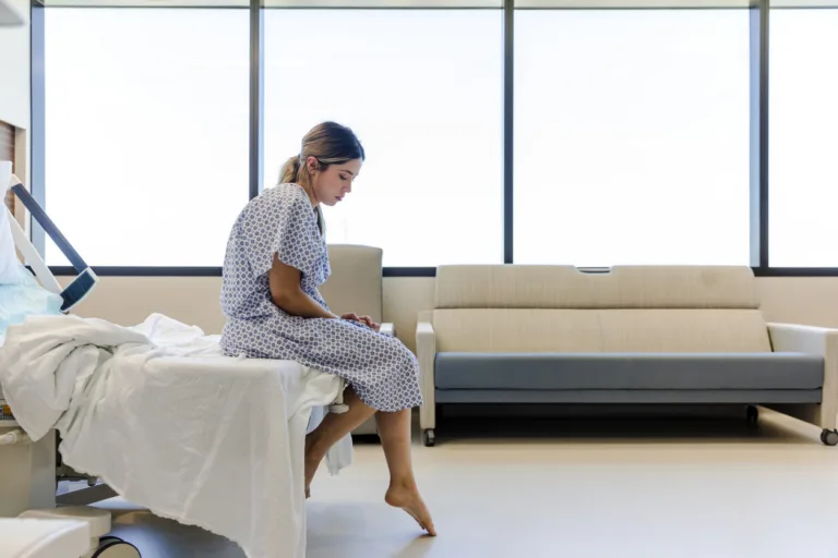 Sitting on the edge of the hospital bed in her hospital gown