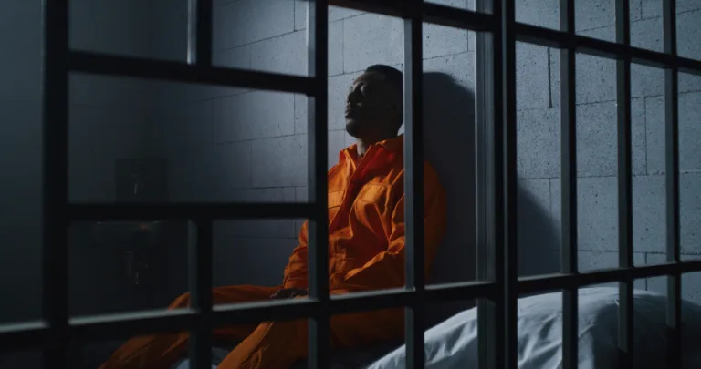 man in orange uniform sits on prison bed