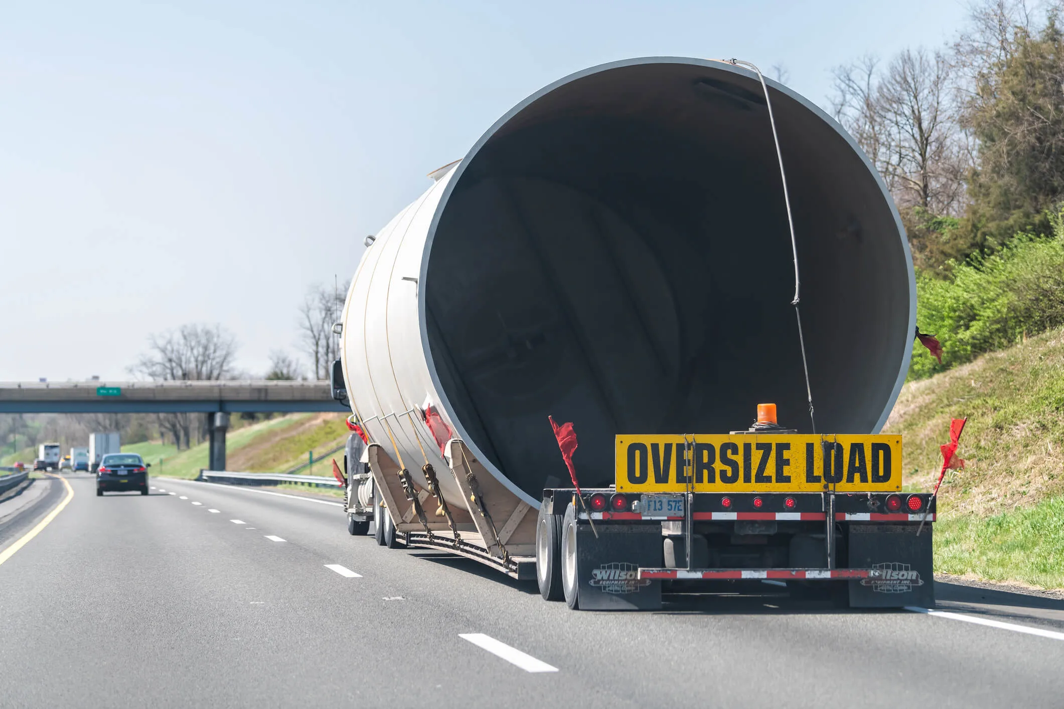 Oversize load hauler truck hauling concrete pipe tube on interstate highway in Virginia with yellow warning signs and red flags
