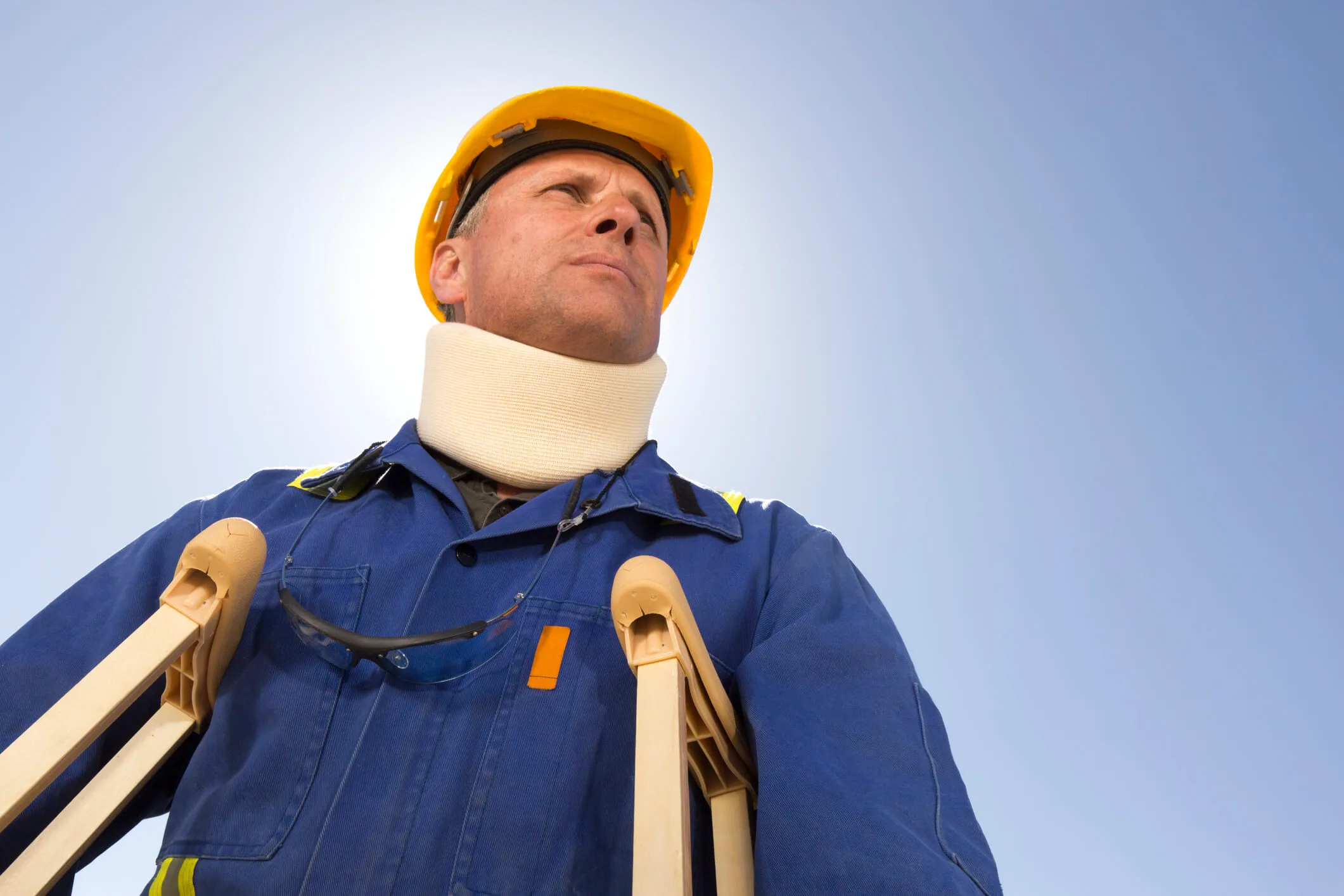 Man wearing construction safety hat and a neck brace standing outside with crutches