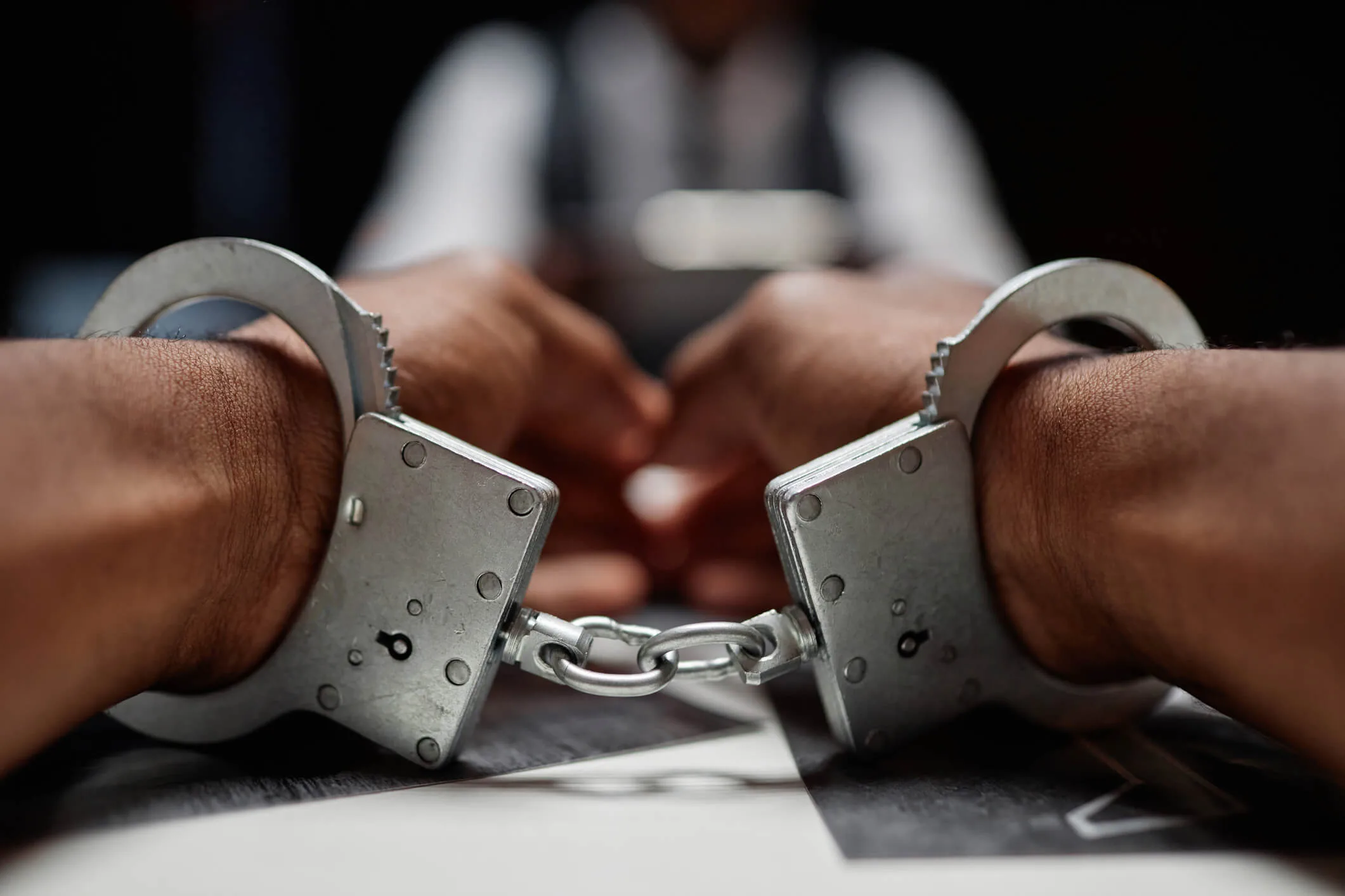 Dramatic close up of Black man wearing handcuffs on hands, criminal suspect